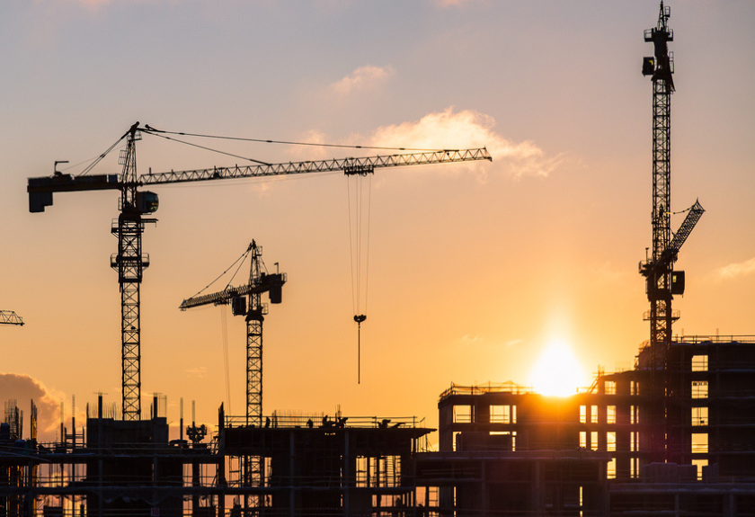 construction cranes in the horizon at the sun sets over toronto skyline