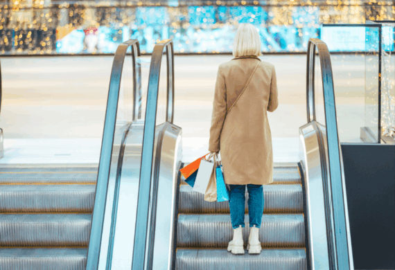 female going up on an escalator carrying several shopping bags